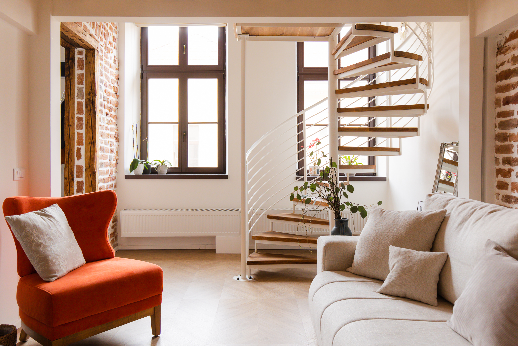 apartament amenajat cu scara in spirala culori neutre si fotoliu portocaliu