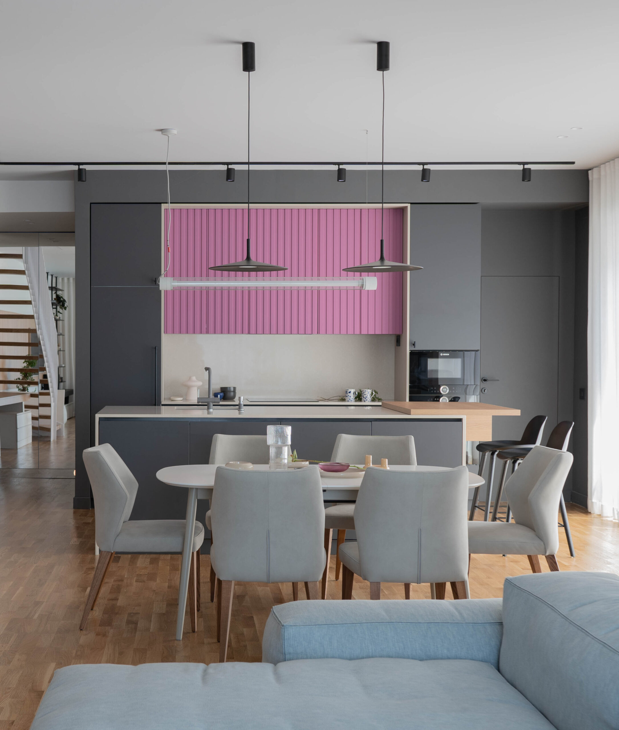 amenajare bucatarie open space gri cu roz insula de bucatarie si zona de dining intre insula si canapea