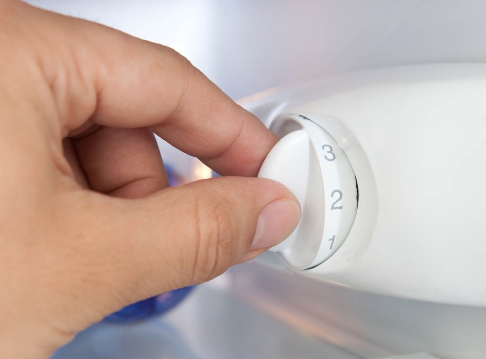 La ce treaptă se ține frigiderul: O mână rotește butonul de setare a temperaturii din interiorul frigiderului.