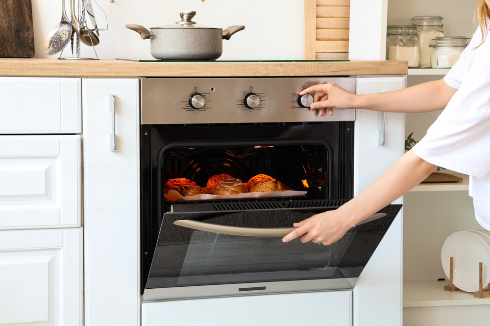 femeie deschide ușa cuptorului electric pentru verifica prăjiturile 