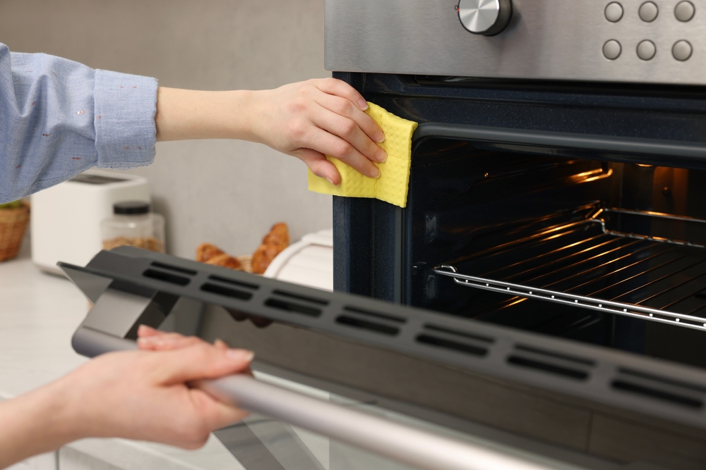 curățare garnituri cuptor electric de către femeie cu cârpă galbena 