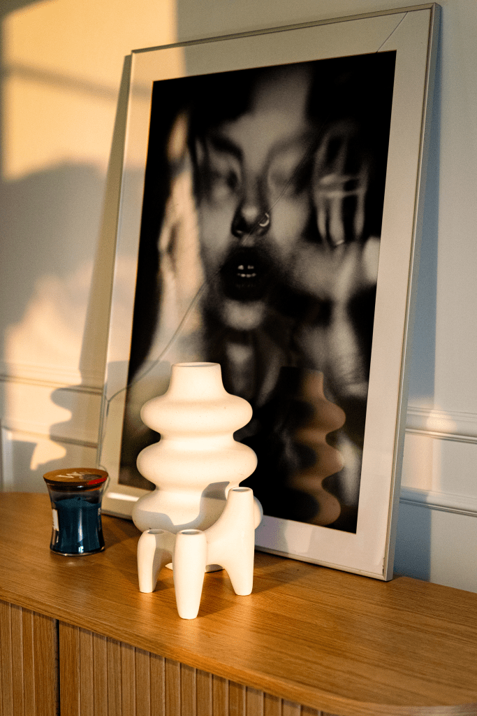 layout cu tablou alb negru, vaza sculpturala si mici decoratiuni asezate pe o comoda din lemn natur