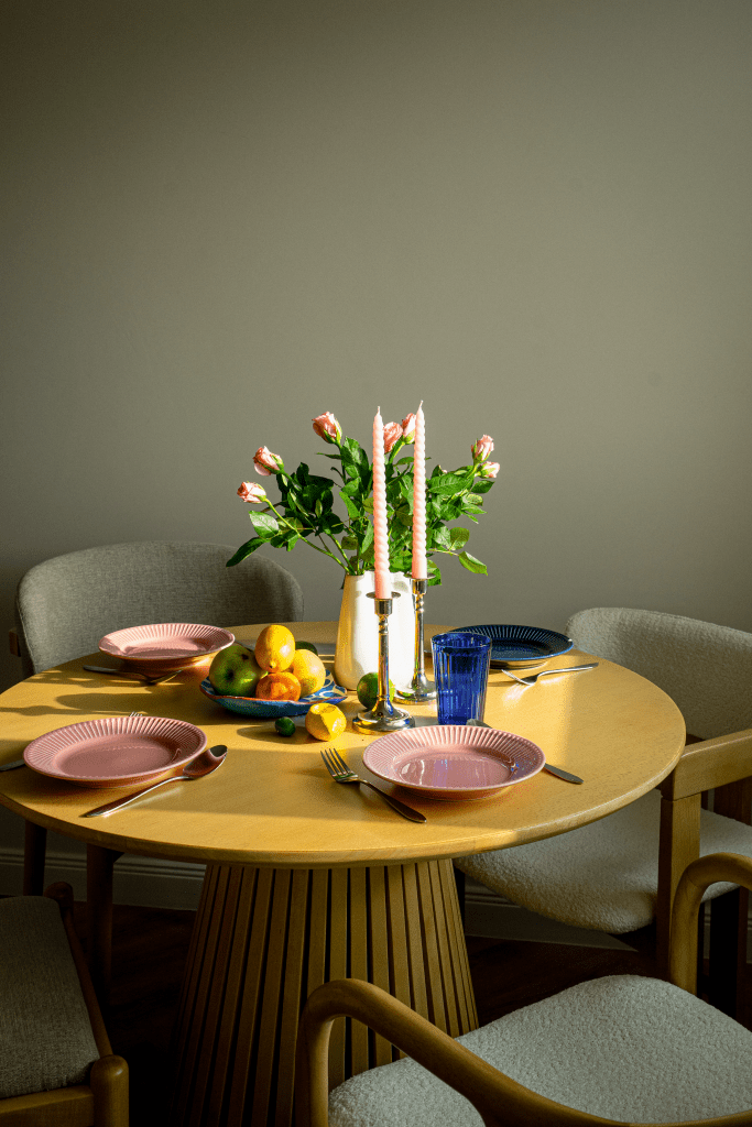 masa de dining din lemn cu scaune tapitate cu boucle alb farfurii din ceramica roz si bleumarin si o vaza cu trandafiri